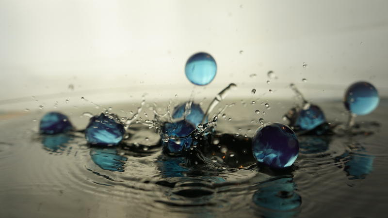 Close-up of several opaque marbles crashing onto a surface of water.