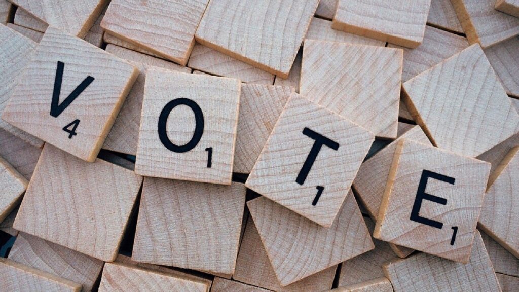 Scrabble tiles spelling out "VOTE" on top of other scattered tiles.