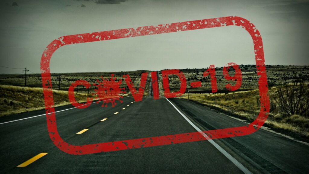 A red stamp reading "COVID-19" in front of an empty road.