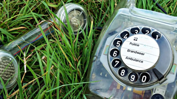 A clear rotary telephone sitting in a patch of long grass.