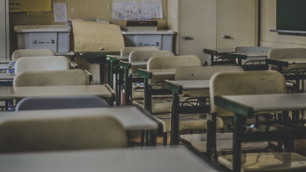 A rustic classroom featuring empty desks and chairs.