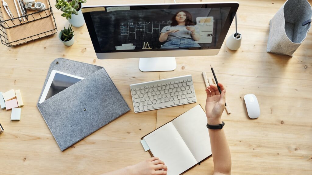 Overhead view of a person at a desk with a notebook in their hand, looking at a computer screen.