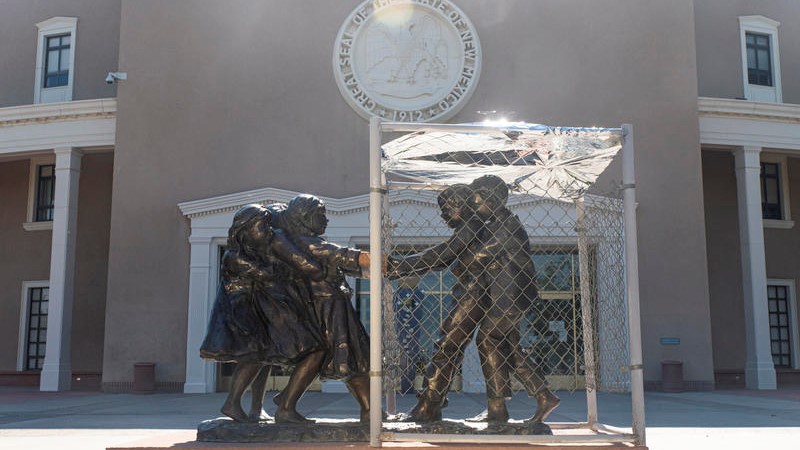 A sculpture in front of the Santa Fe Roundhouse depicting two groups of children tugging at each other, with a metal cage placed on top of one of the groups.