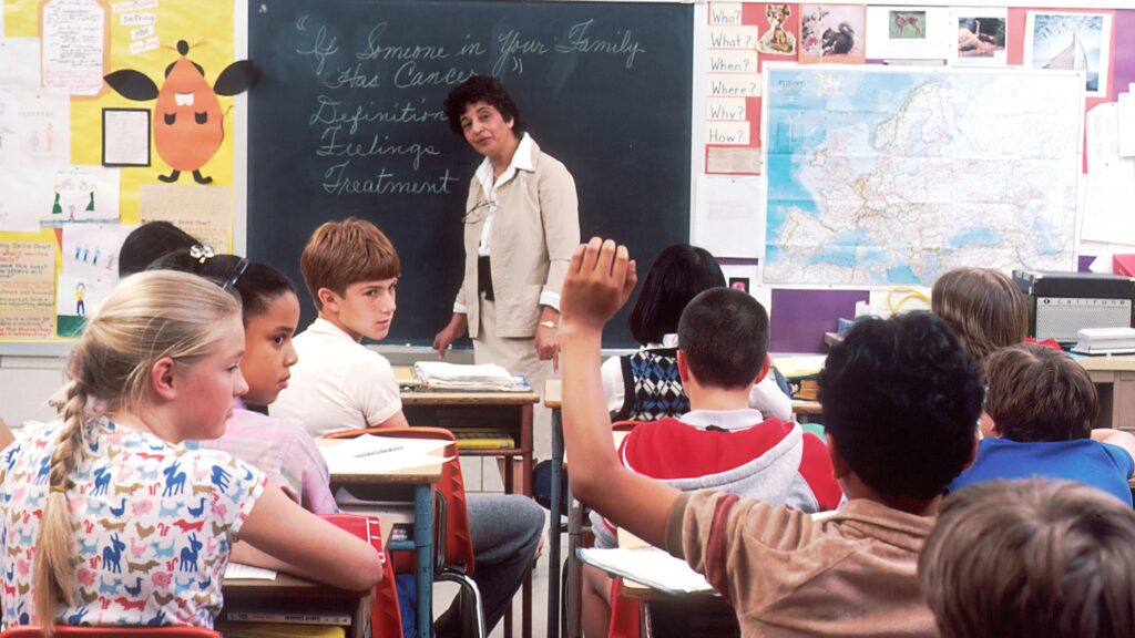 A student raises their hand in a full classroom.