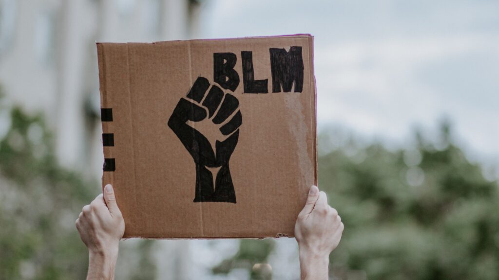 Hands hold up a cardboard sign with a fist drawn on and the text "BLM".