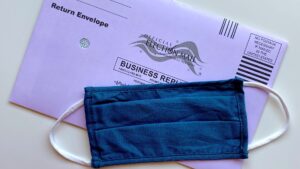 A mail ballot's return slip, with a facemask lying on top of it.