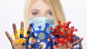 A person in a facemask holds up their hands, with superimposed graphics of coronaviruses.