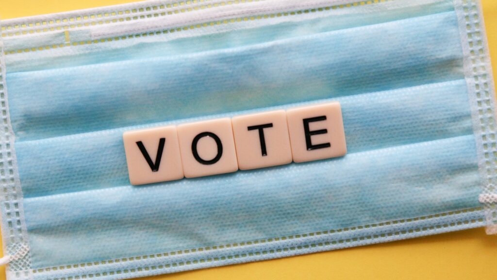 A surgical mask with Scrabble tiles placed on top spelling out "VOTE".