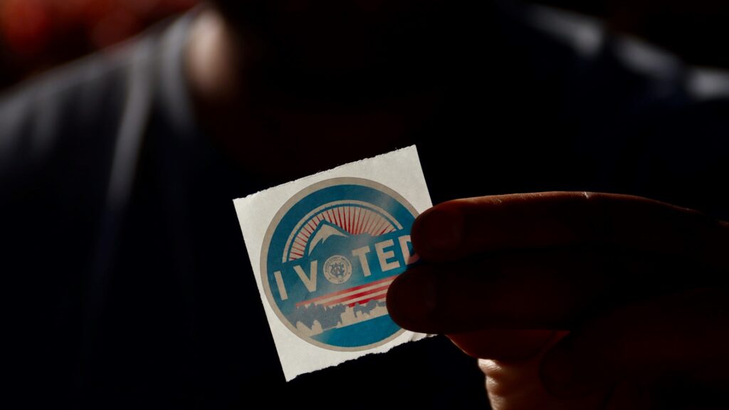 A hand holds an "I VOTED" sticker.