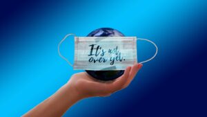 A hand holds a small globe with a facemask over it, with text reading "It's not over yet."