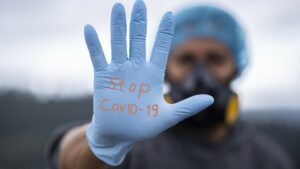 A medic wearing a gas mask holds up a gloved hand with writing "Stop COVID-19".