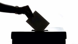 Silhouette of a hand placing a ballot into a box.