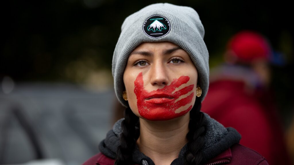 A demonstrator looks past camera, with a red handprint covering their mouth.