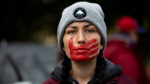 A demonstrator looks past camera, with a red handprint covering their mouth.