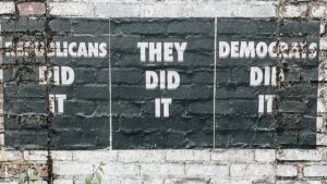 Signs printed on a brick wall reading "REPUBLICANS DID IT", "DEMOCRATS DID IT" and "THEY DID IT" in the center.