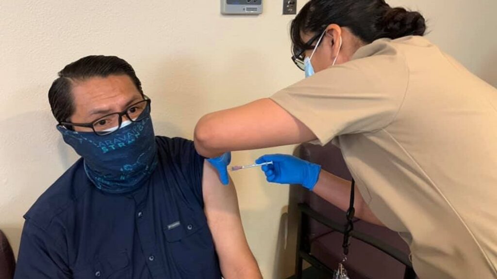 A man wearing a gaiter gets injected with a syringe.