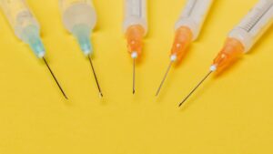 Close-up of the ends of five syringes atop a yellow backdrop.