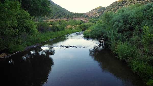 A body of water flanked by greenery and rocky hills in the background.