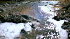 An icy body of water flanked by rocks and mud.