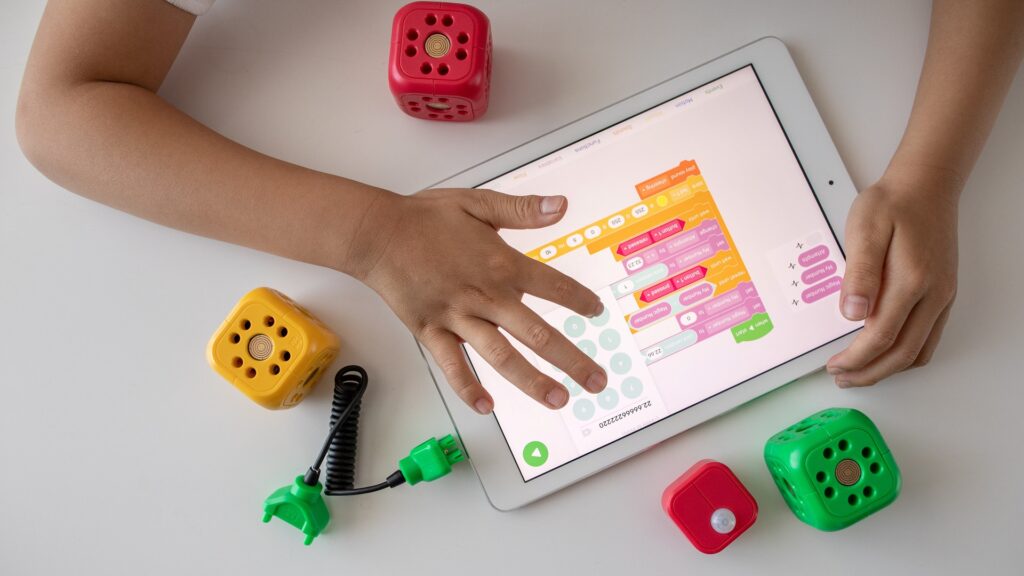 A child's arms play with a tablet and other toys on a table.