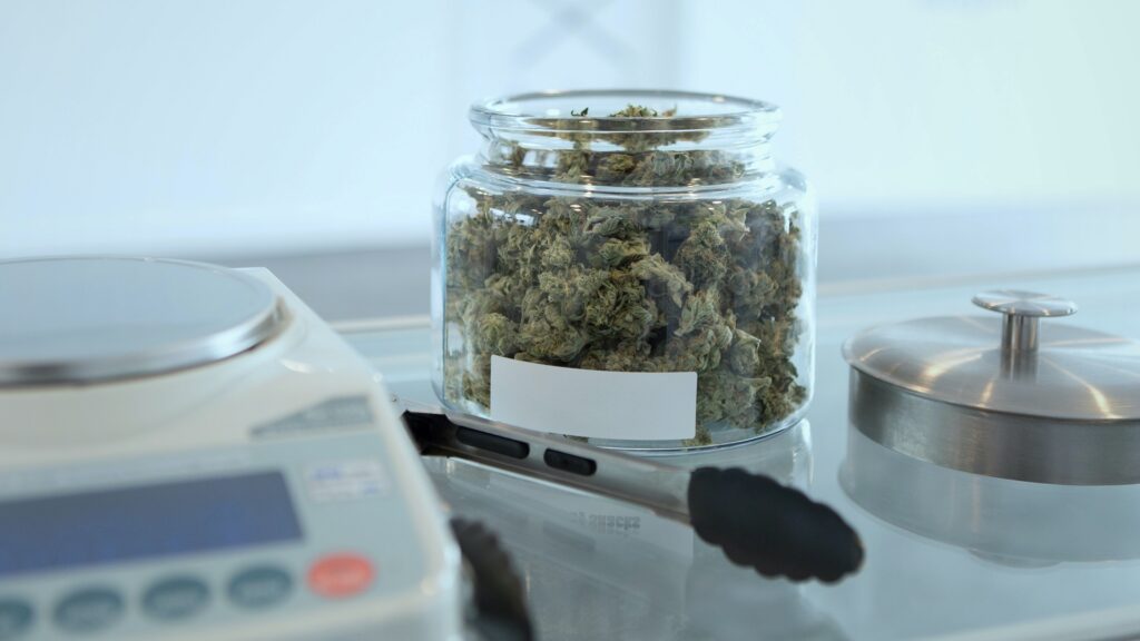 Cannabis colas in a glass jar, next to tongs and a digital scale.