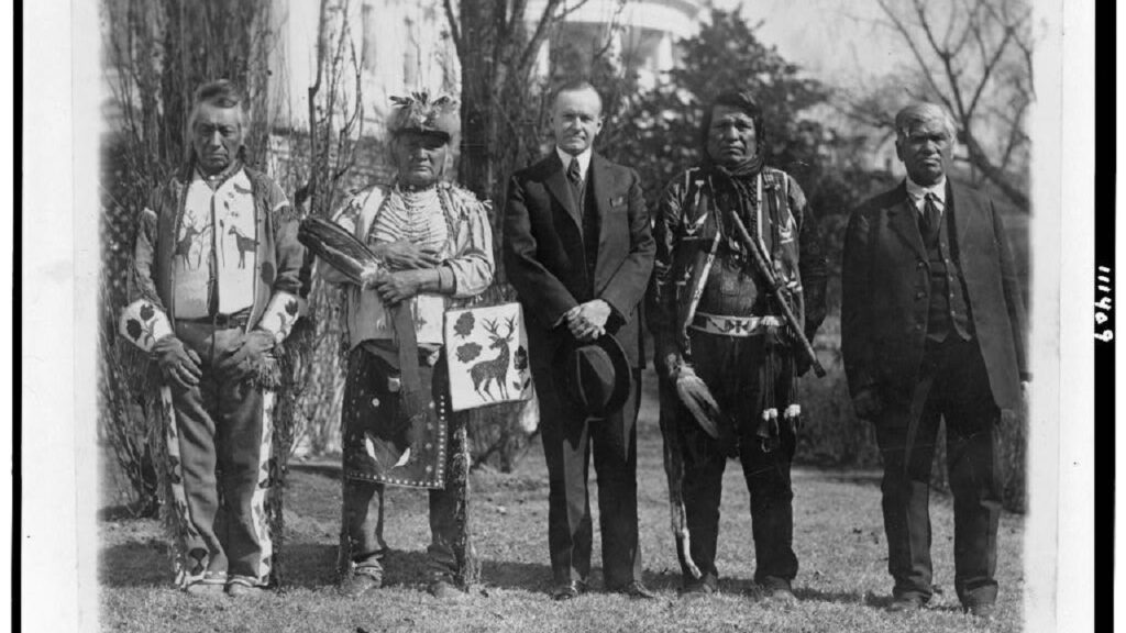 Native men and a white man stand next to each other for an antique photo.