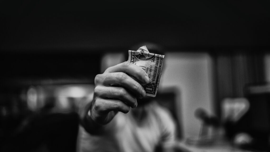 A hand holds up a crumpled $1 dollar bill.