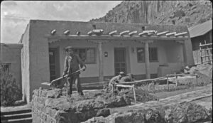 Antique photograph of three people working in the front yard of an adobe house.