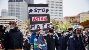 A protestor holds up a sign reading "#STOP ASIAN HATE" in a city square.