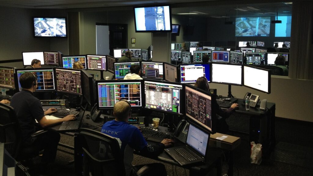 Control room for spaceflight, with several people sitting in front of busy computer monitors.