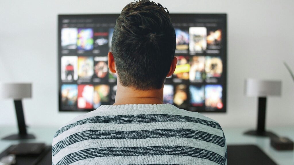 A person sits in front of a television screen, selecting from a gallery of titles.