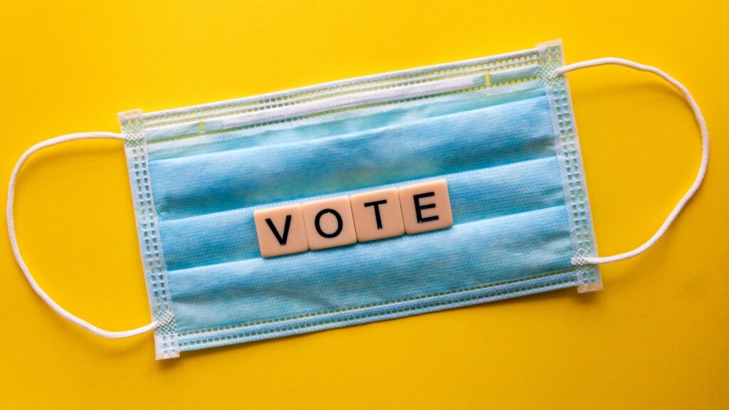 A facemask laid down on a surface with Scrabble tiles on top reading "VOTE".