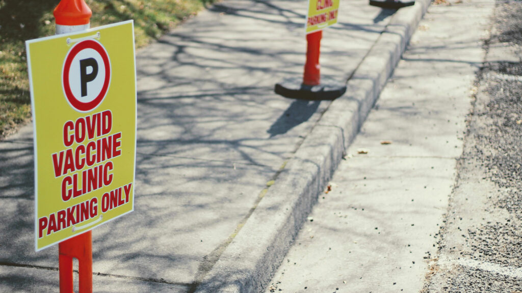 Parking cone with sign attached to it reading "COVID VACCINE CLINIC - PARKING ONLY".