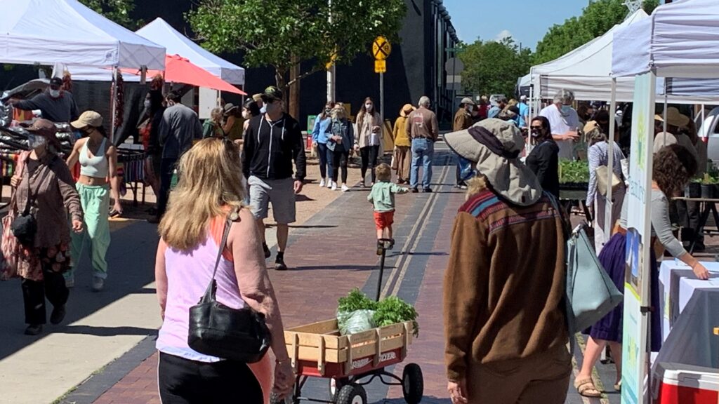 People wearing facemasks walk through a corridor of a farmers' market.