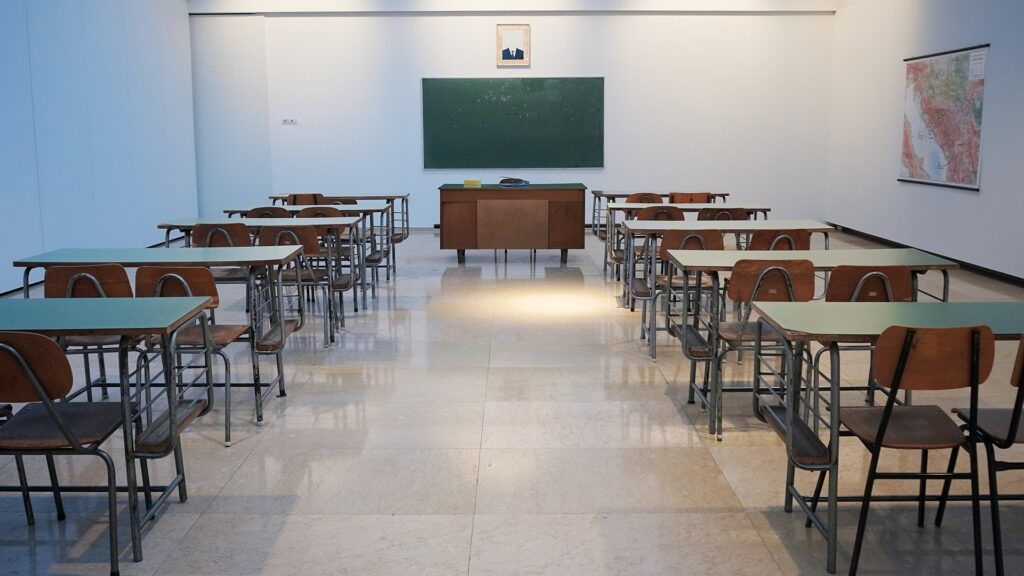 An empty classroom with desks and a chalk board on the wall.
