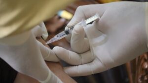 A pair of gloved hands administering a vaccine with a needle.