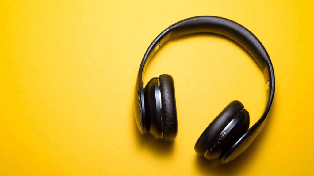 A pair of wireless headphones laying on a yellow backdrop.