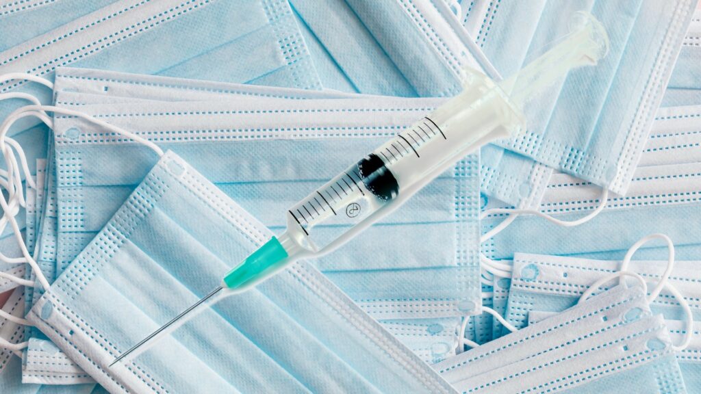 A syringe on top of a pile of blue surgical masks.