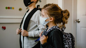 Two children wearing masks with backpacks on.