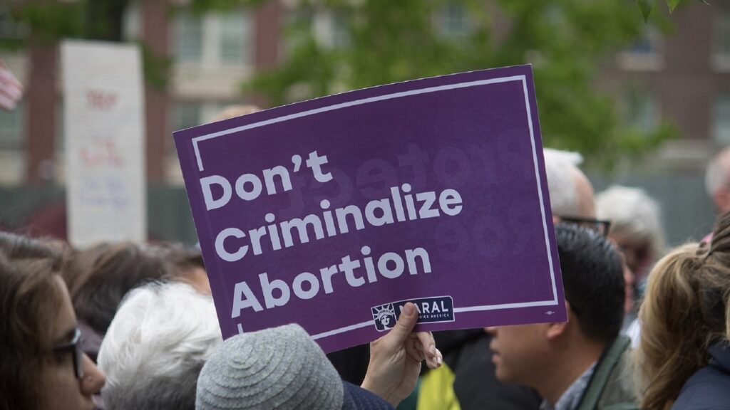 A crowd of people and a sign being held up that say "Don't Criminalize Abortion"
