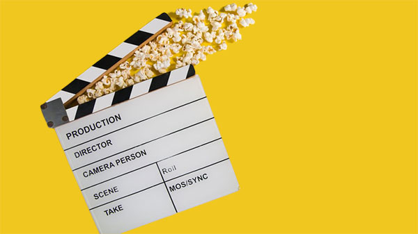 A film slate or clapper with popcorn coming out of the top on a yellow background