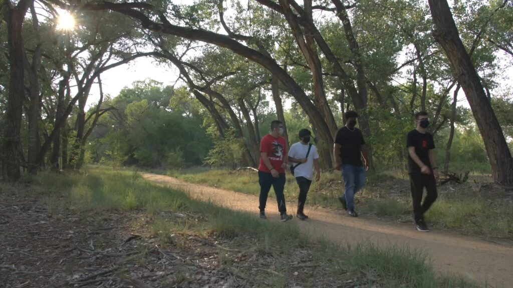 4 people walk along a path in a forested area