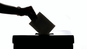 A silhouette of a person placing their voting ballot into a box
