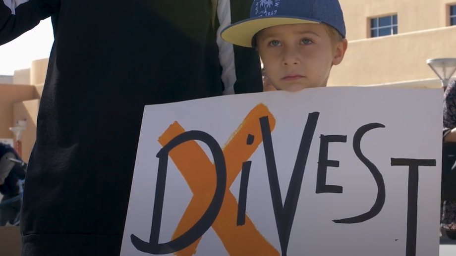 A small child holding a sign that says Divest with a x on it.