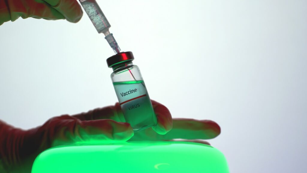 A person filling a syringe with the COVID-19 vaccine illuminated by a green light underneath