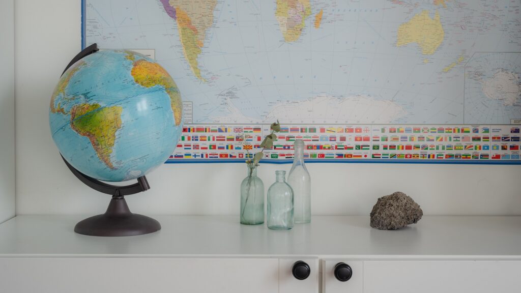 A desk in a classroom with maps, a globe, some glass bottles and a rock