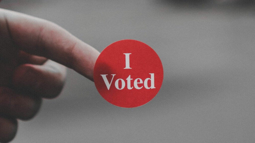 A person with a red "I Voted" sticker on the tip of their finger
