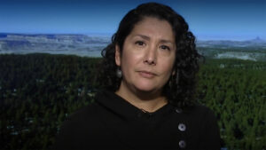 Valerie Rangel sits for an interview in front of a screen with a landscape displayed on it.
