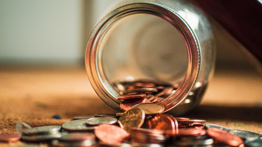 A mason jar tipped over with coins spilling out.