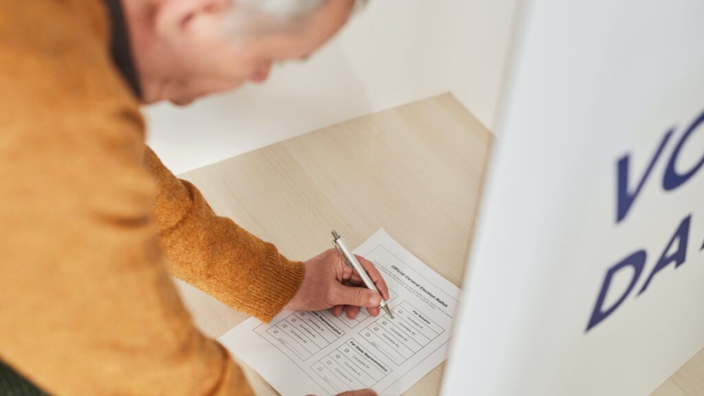 An older man bending down to fillout a voting ballot.